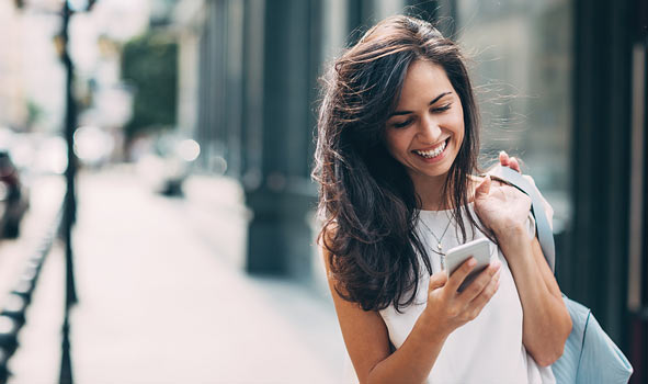 a woman standing on the street smiling at a phone