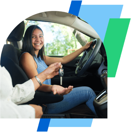 a young woman sits in a car and smiles as another person hands her a key