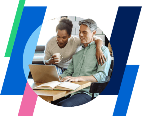 a man and a woman look at a laptop while the woman holds a coffee mug